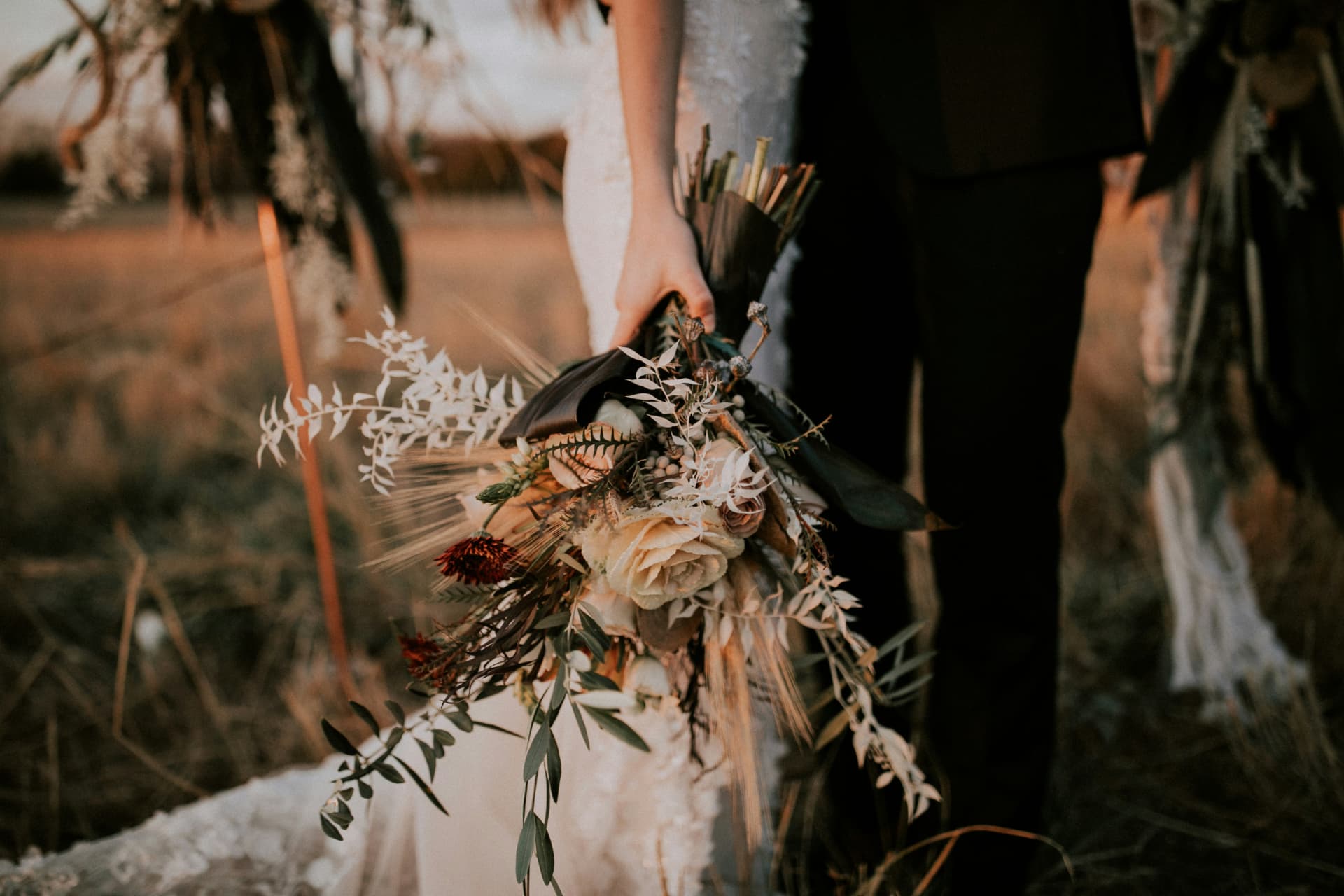 Bride holding a dried-floral wedding bouquet beside her partner at sunset